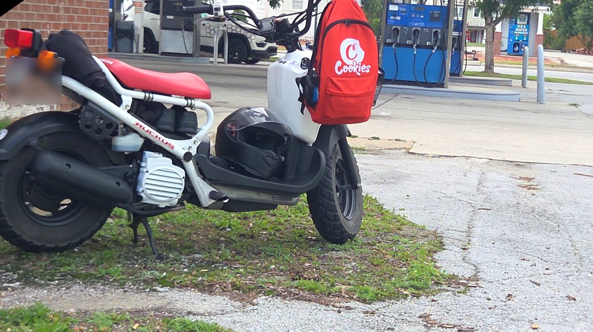 White and red Honda Ruckus with a red delivery bag, parked at a New Bern gas station